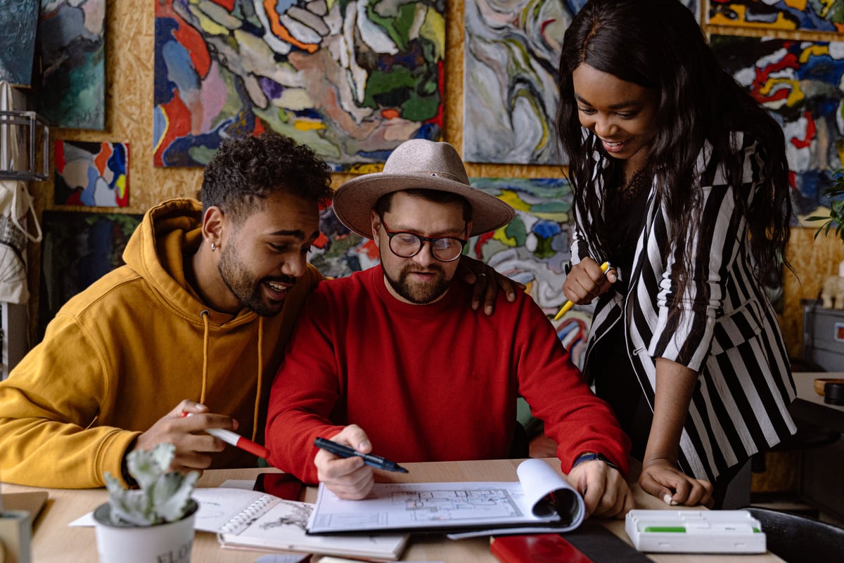 Men and Woman Discussing Project in a Sketchbook and Abstract Paintings Hanging on a Wall